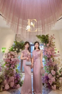 婆婆與岳母在婚禮現場身穿艾莉粉色系列手工主婚人禮服，於花藝背板前優雅合影