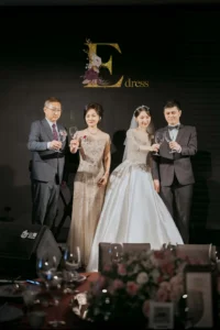 為什麼婚禮媽媽禮服都推薦珠工款?5大原因一次看懂 4 婚宴舞台上主婚媽媽穿香檳色珠工禮服與新人合照,舞台燈光呈現珠工細節與質感